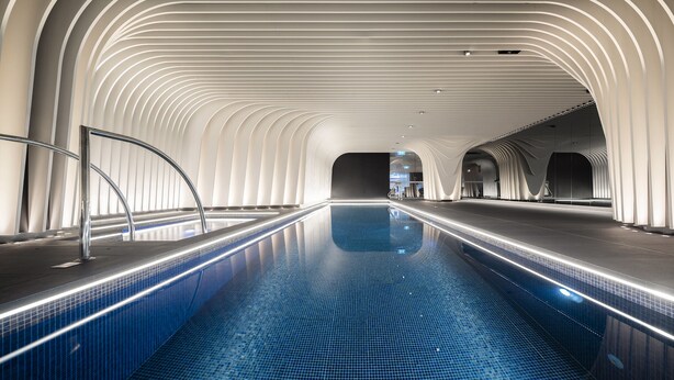 A modern indoor swimming pool with a sleek, curved ceiling design and a clear, blue pool. - SKYE Suites Sydney (Sydney)