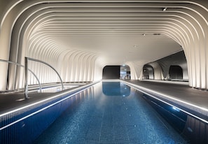 A modern indoor swimming pool with a sleek, curved ceiling design and a clear, blue pool.