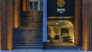 A modern hotel entrance with a staircase leading up to a glass door, a prominent sign reading "SKYE SUITES", and a view into the interior with seating areas. - SKYE Suites Sydney (Sydney)