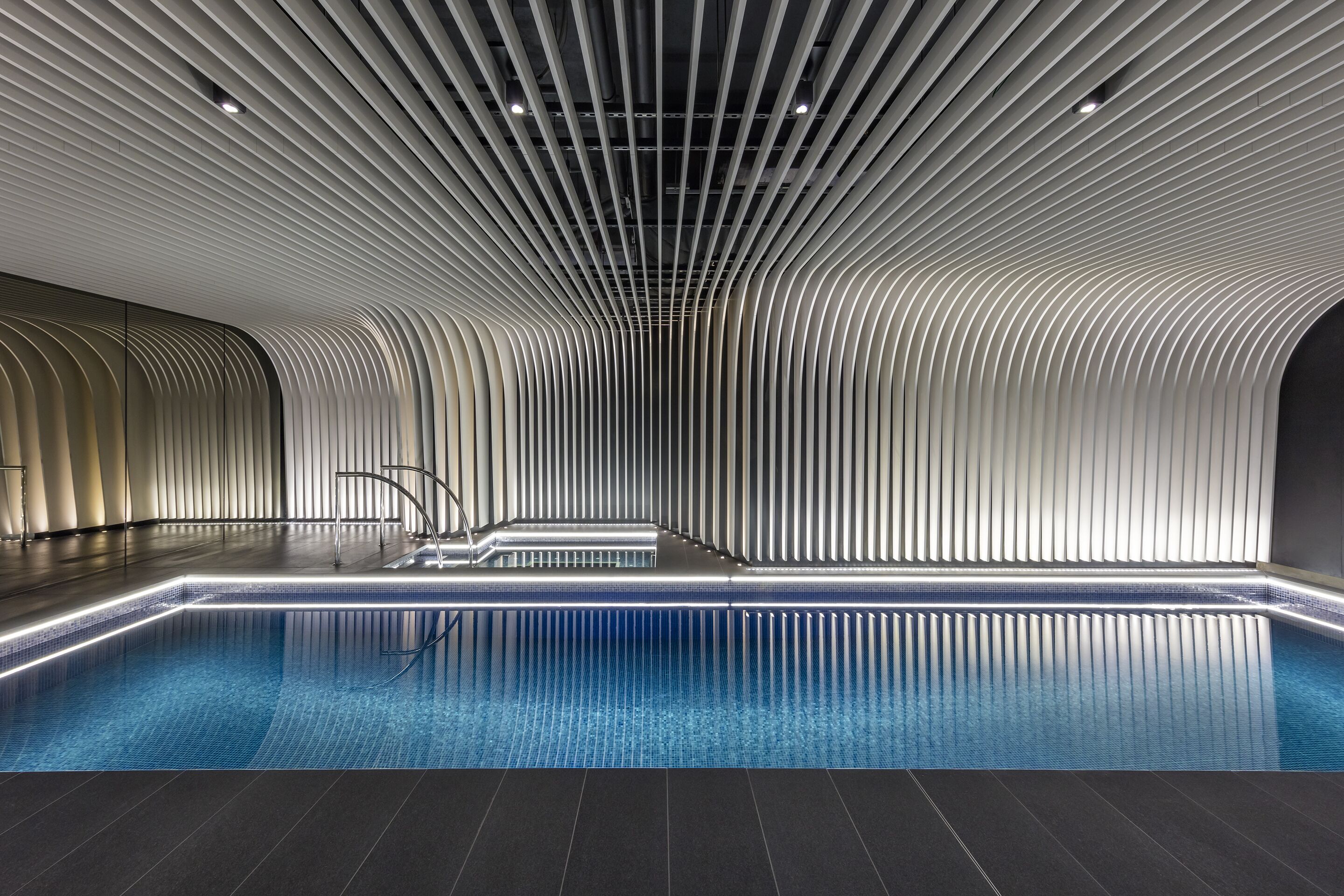 A modern indoor swimming pool with a sleek, curved ceiling and a minimalist design.