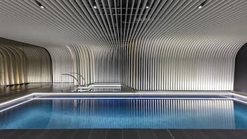 A modern indoor swimming pool with a sleek, curved ceiling and a minimalist design.