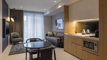 A modern kitchen with a dining area, a sofa, and a TV mounted on the wall.