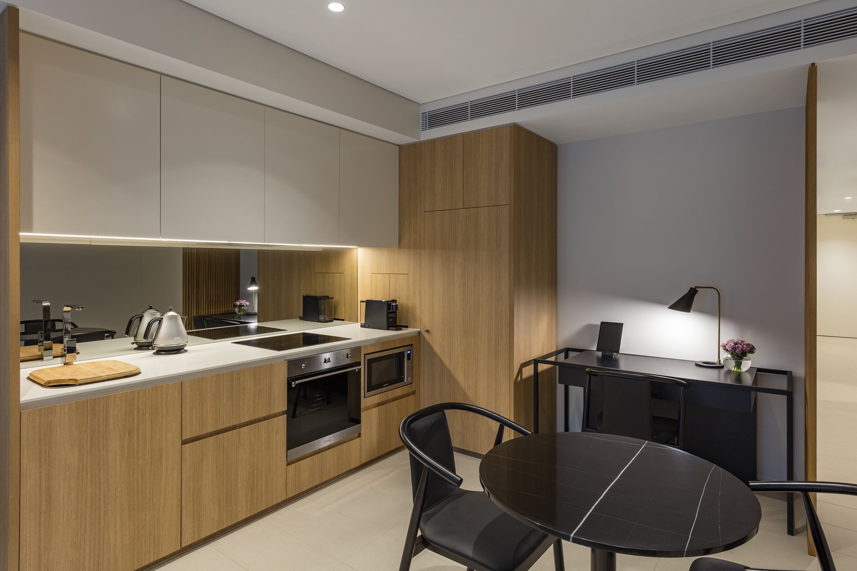 A modern kitchen with a central island, built-in oven, microwave, and a dining area with a round table and chairs.