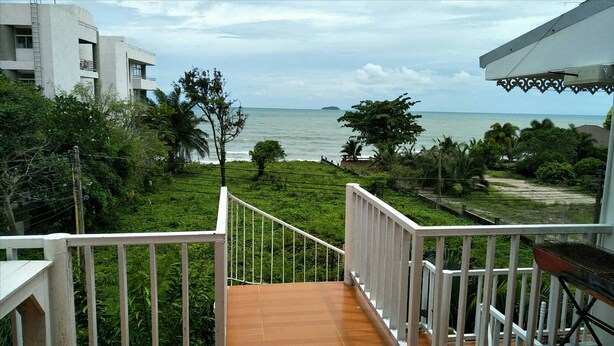 A balcony with a view of the ocean, surrounded by greenery and a white building. - White House Mountian Beach Resort (Klaeng)
