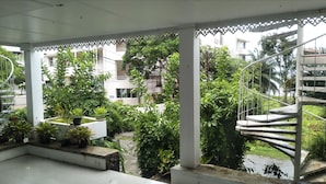A covered outdoor area with a spiral staircase, potted plants, and a view of surrounding buildings. - White House Mountian Beach Resort (Klaeng)