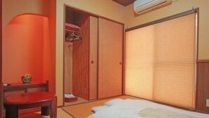 Une pièce de style japonais traditionnel, avec un sol recouvert de tatamis, un futon servant de lit, une armoire en bois et une porte coulissante dotée de stores.