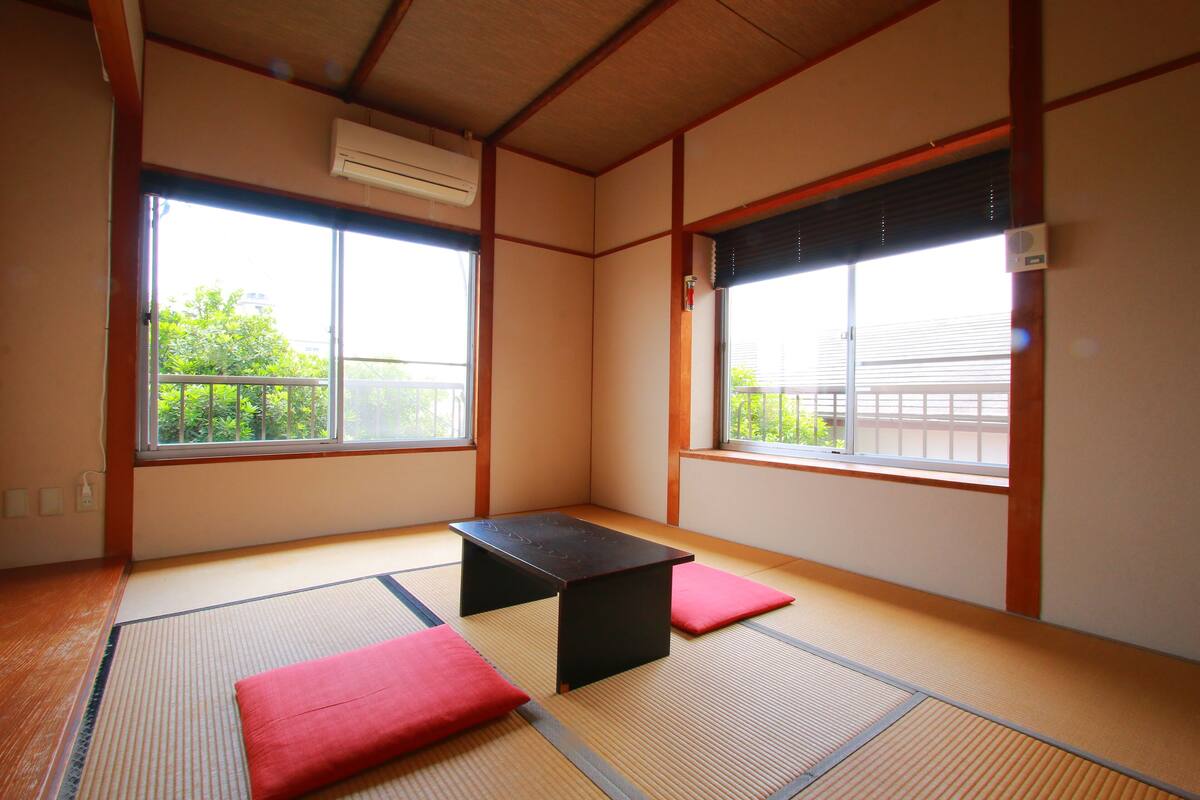 A tatami mat room with a low table and cushions, large windows, and an air conditioning unit.