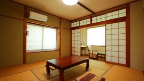 Une pièce de style japonais traditionnel, avec un sol recouvert de tatamis, une petite table en bois, des portes coulissantes en papier de riz (shoji) et un ventilateur de plafond.