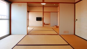 Une pièce de style japonais traditionnel, avec un sol recouvert de tatamis, des portes coulissantes et un téléviseur.