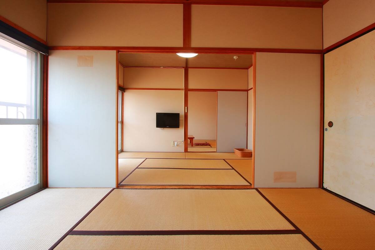 A traditional Japanese room with tatami flooring, sliding doors, and a television.
