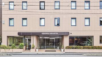 A URAYASU SUN HOTEL with a modern facade, multiple windows, and a well-maintained entrance area with potted plants.