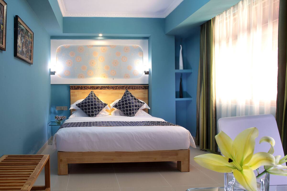 A bedroom with a bed, bedside tables, a nightstand, a chair, and a window with curtains.