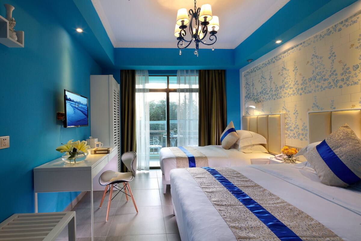 A hotel room with two beds, a desk, a chair, a TV, and a balcony with a view.