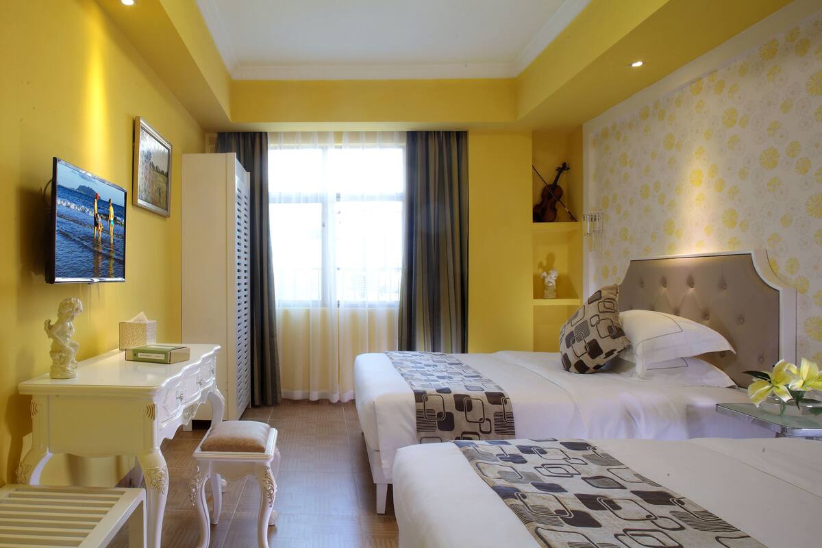 A hotel room with two beds, a desk, a chair, and a TV.