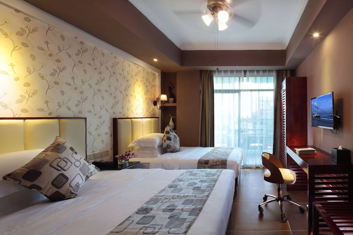 A hotel room with two beds, a desk, a chair, a television, and a window with curtains.