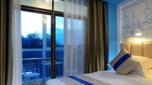 Quarto de hotel com uma cama grande, uma varanda com uma cadeira e vista para árvores.