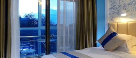 A hotel room with a large bed, a balcony with a chair, and a view of trees.
