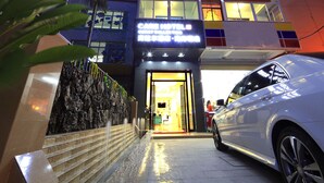 Entrada de hotel com fachada moderna, um elemento aquático visível e um carro estacionado em frente.
