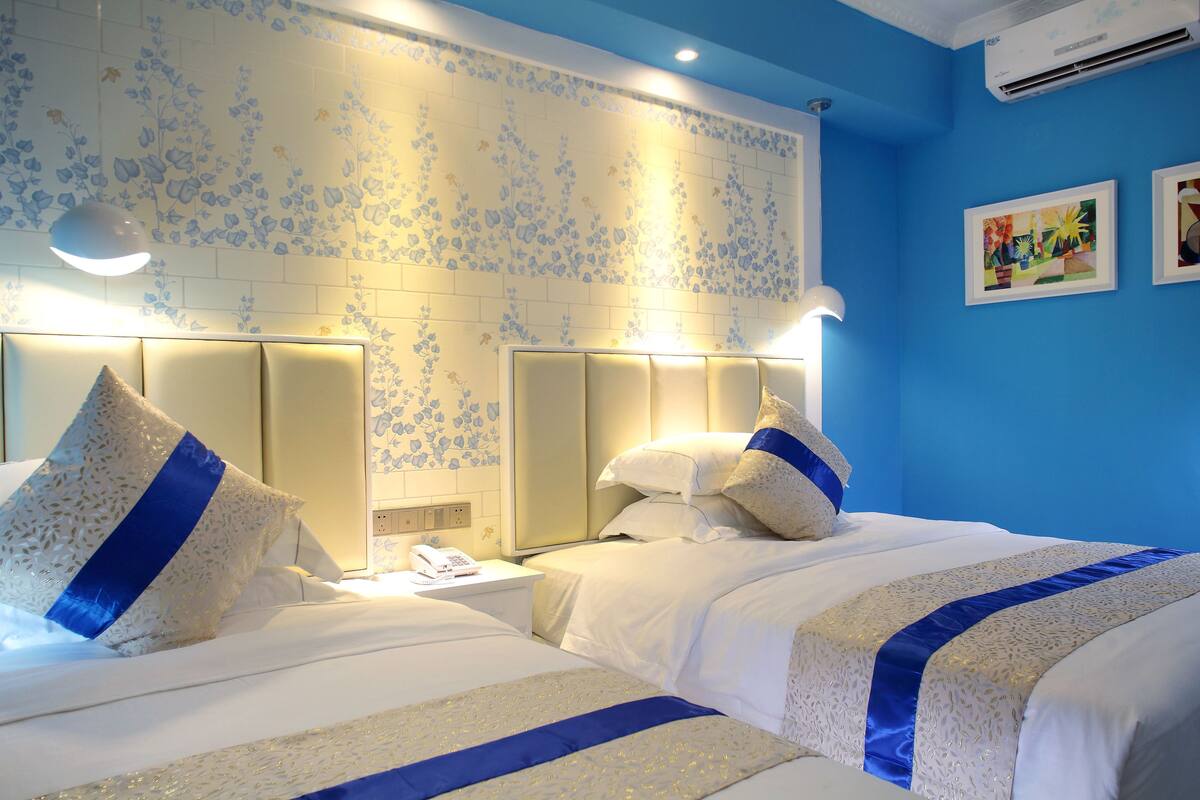 A hotel room with two beds, a floral-patterned wall, and a blue accent wall.