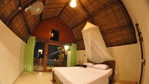 Une chambre à coucher avec un lit, un ventilateur de plafond, une fenêtre avec des rideaux et une petite lampe de chevet.