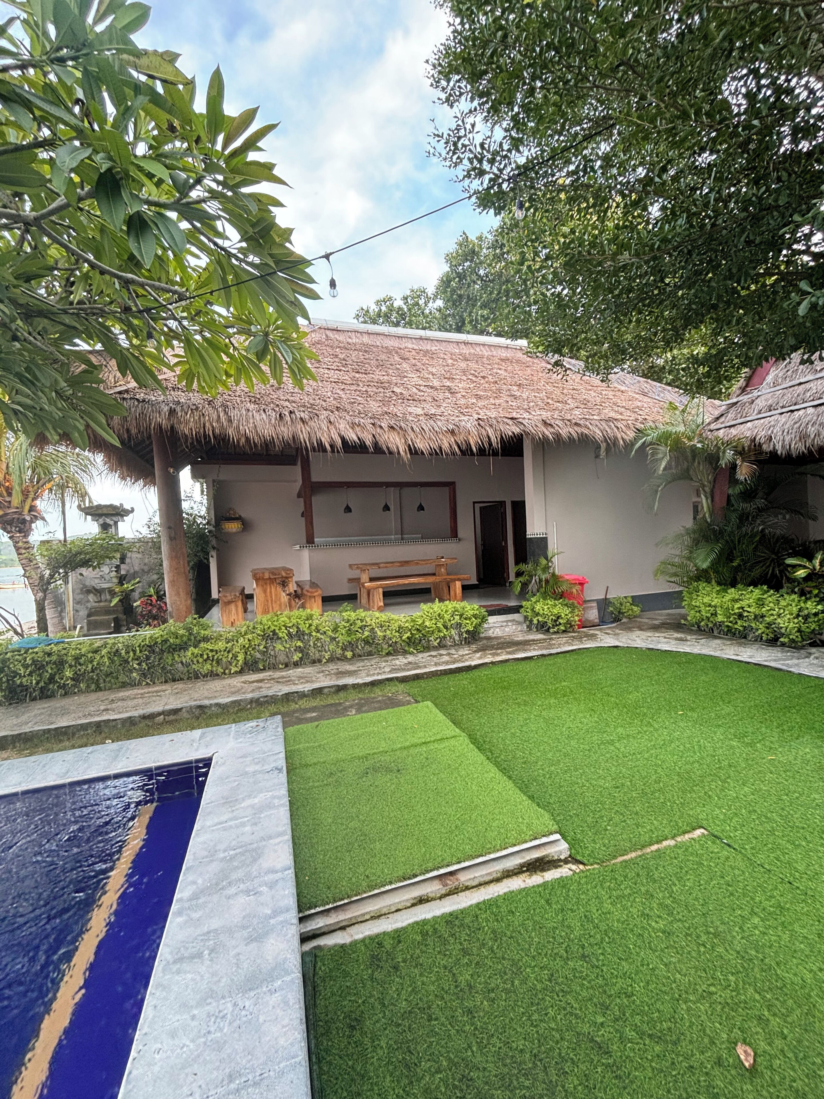 A thatched-roof building with a small lawn and a pool.