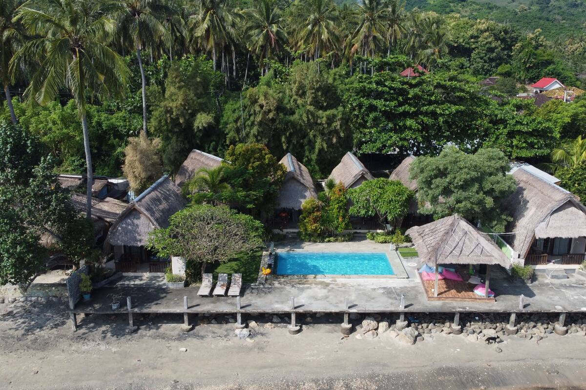 Un resort con cabañas de techo de paja, piscina y exuberante follaje.