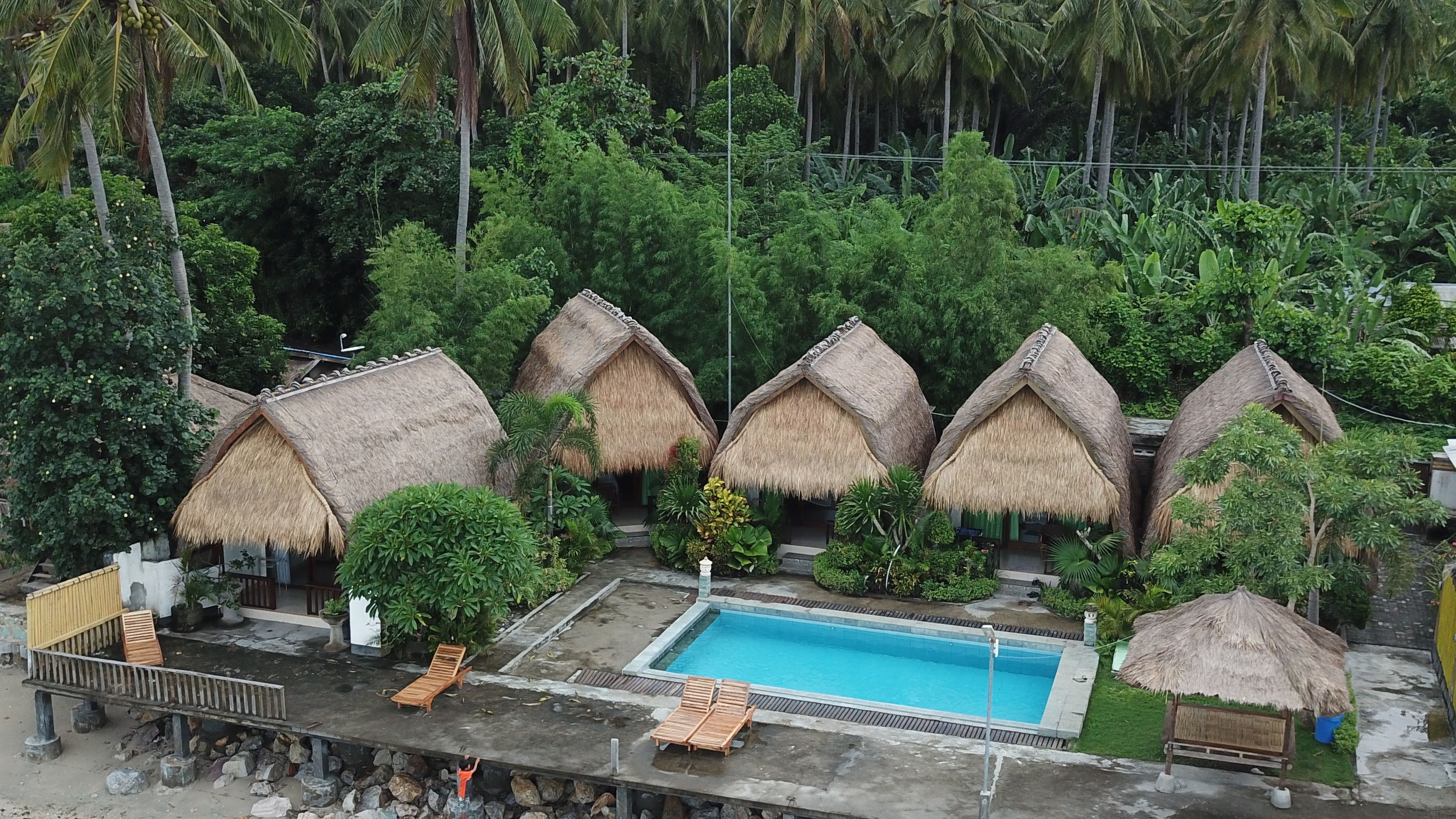 Un resort con cabañas de techo de paja, piscina y abundante vegetación.