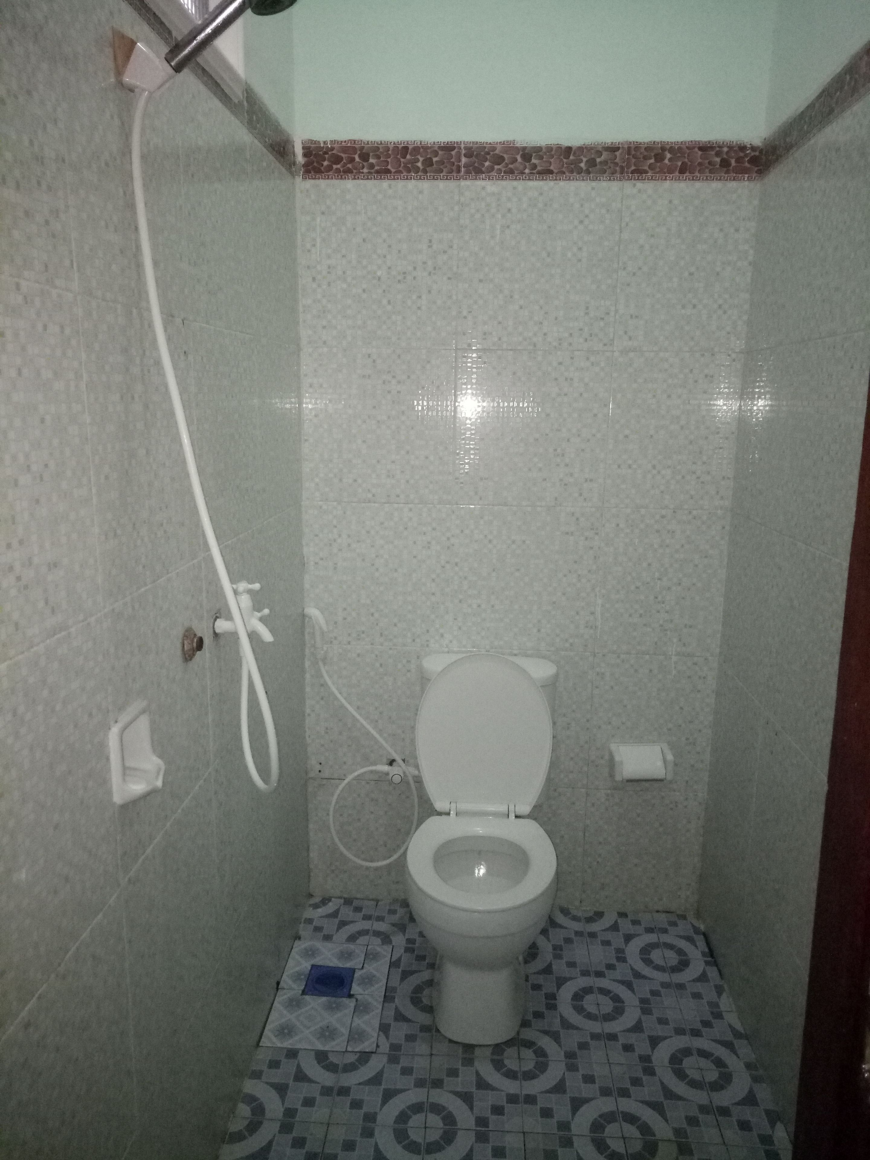 Un baño pequeño con inodoro, ducha y piso estampado.