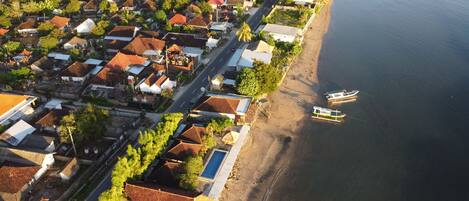 An aerial view of a coastal village with traditional houses, a main road, and boats docked near the shore.