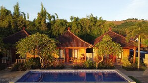 Une villa de style traditionnel dotée d’une piscine, entourée d’une végétation luxuriante et de collines.