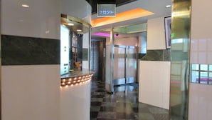 Un vestíbulo de hotel con mostrador de recepción, un ascensor de vidrio y una señal que indica un piso.