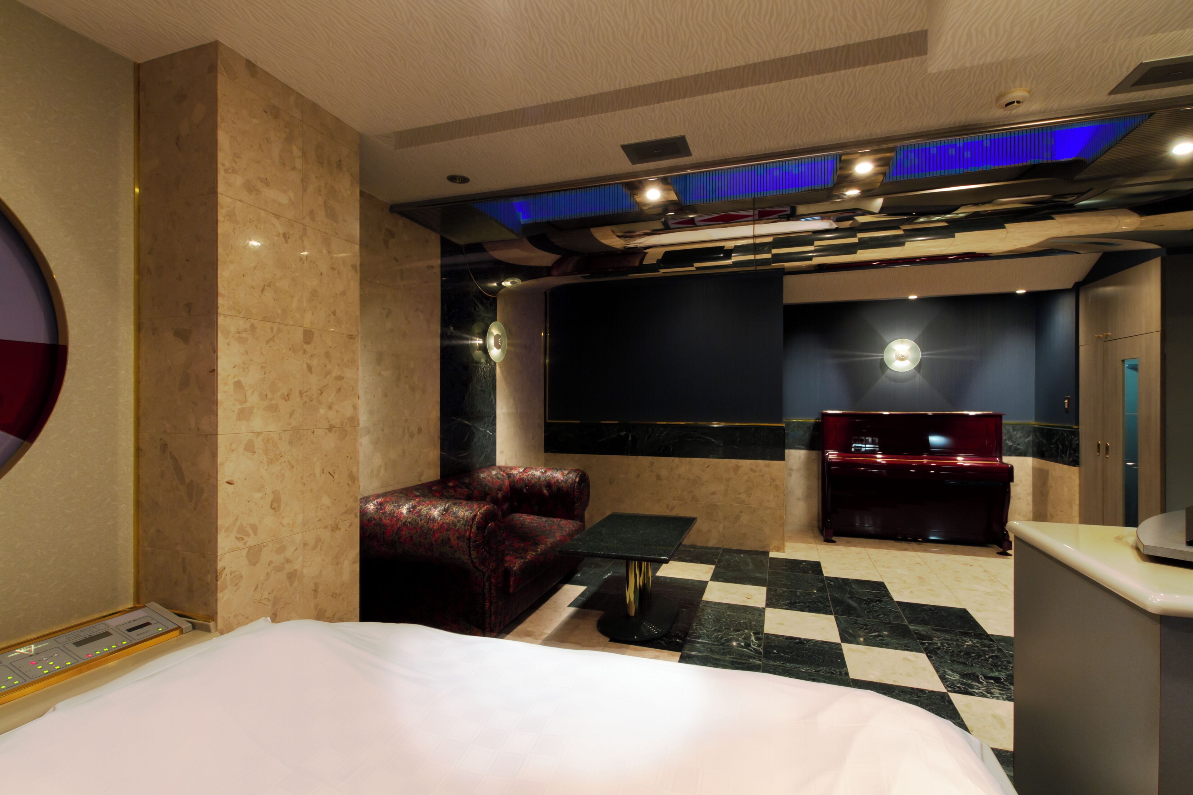 A hotel room with a bed, a red sofa, a black coffee table, a minibar, and a checkered floor.