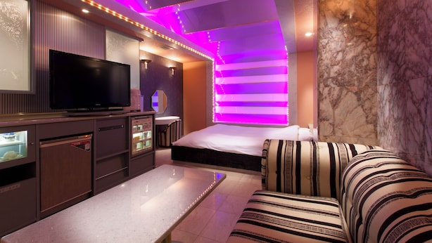 Una habitación de hotel moderna con una televisión de pantalla plana, una cama, un sofá y una pared de acento de mármol.