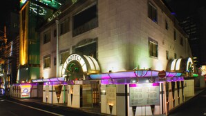 Un hotel con un letrero de neón, un acceso cubierto y una señalización con información.