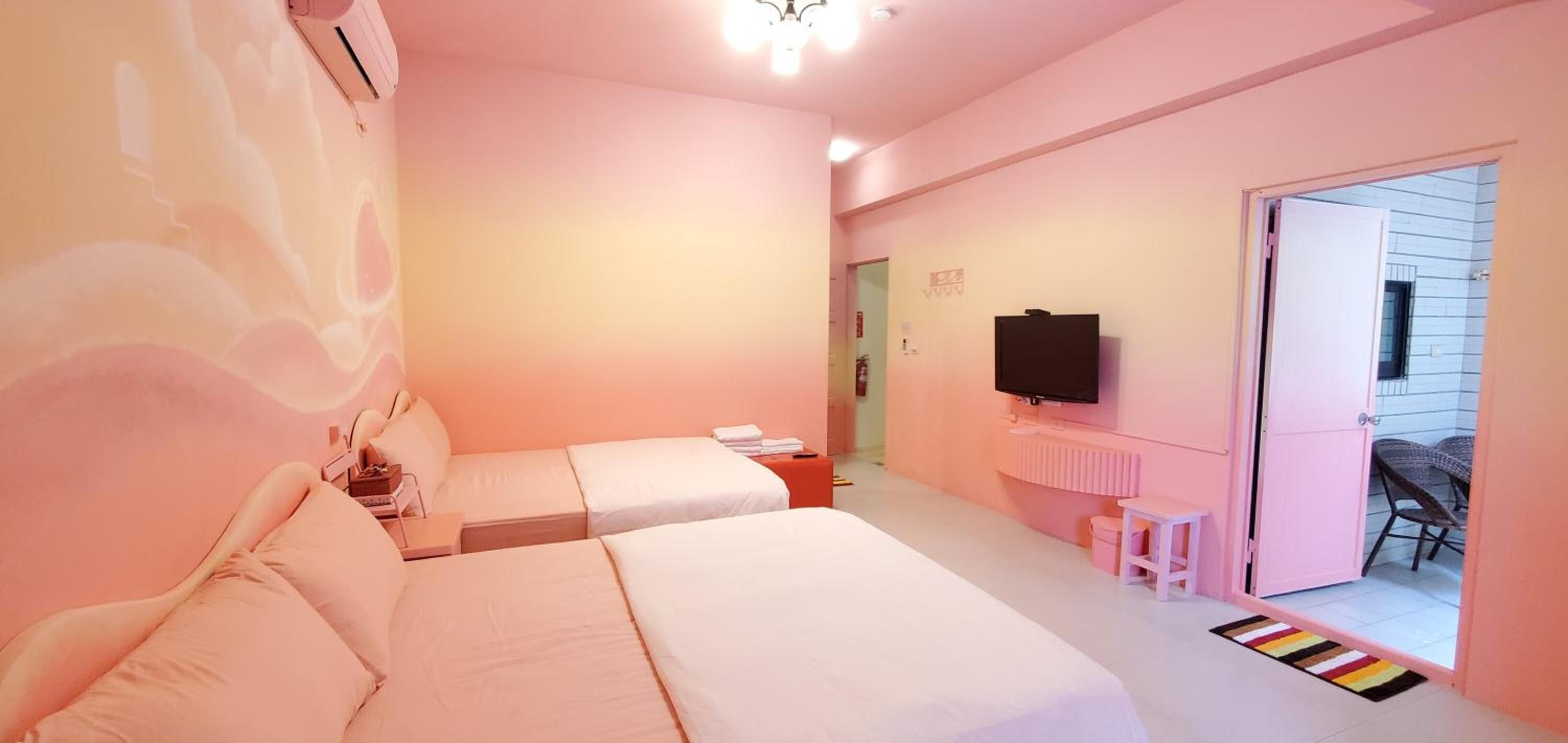 A pink-themed hotel room with two beds, a TV, and a small table.