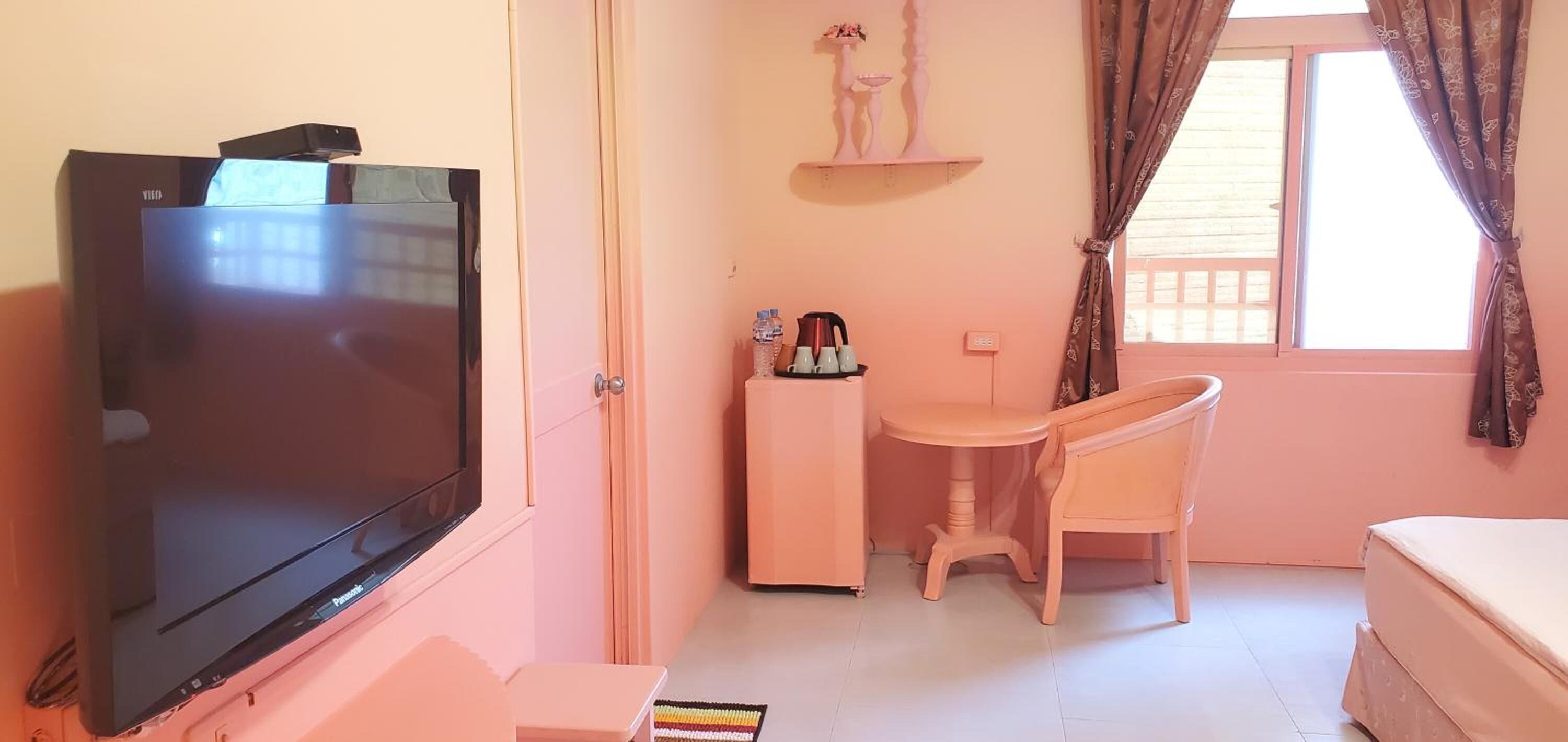 Una habitación pequeña con televisión, escritorio, silla, cama y ventana con cortinas.