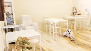 A room with white furniture, including a table and chairs, a white sofa, and a small dog on the floor. - DingDing Home (Hengchun)