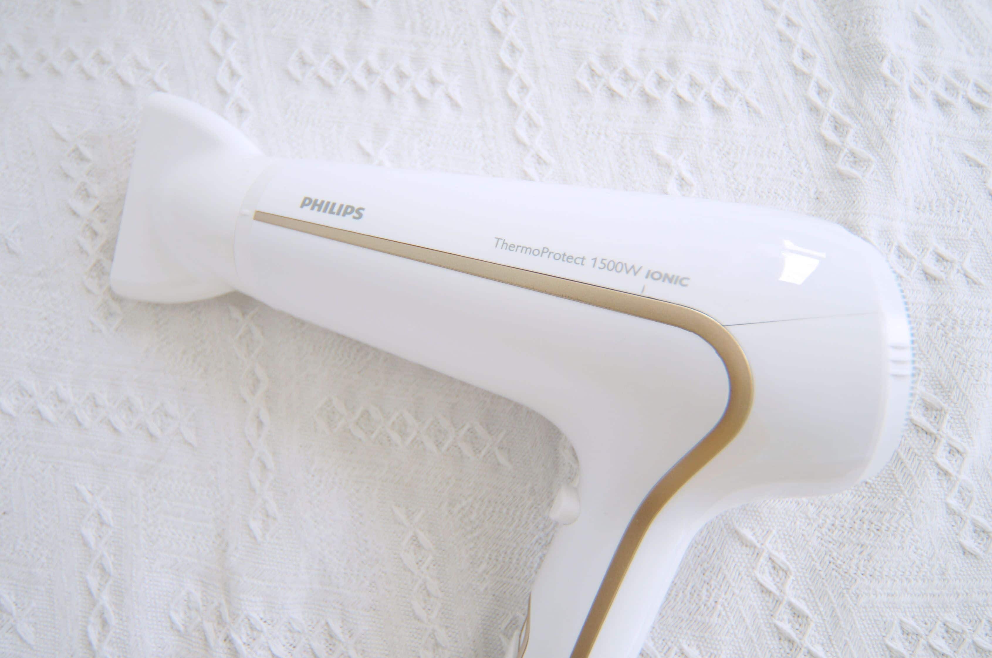 A Philips hair dryer with a gold accent on a white textured surface.