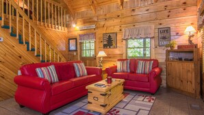 A cabin interior with two red sofas, a wooden chest, and a staircase. - Secluded,-Private,Free WIFI,Pool Table,Hot Tub, Jacuzzi, 400 Game Arcade  (Pigeon Forge)