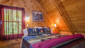 A cozy wooden cabin bedroom with a bed, pillows, a quilt, a window with curtains, a wall-mounted picture, and a lamp. - Secluded,-Private,Free WIFI,Pool Table,Hot Tub, Jacuzzi, 400 Game Arcade  (Pigeon Forge)