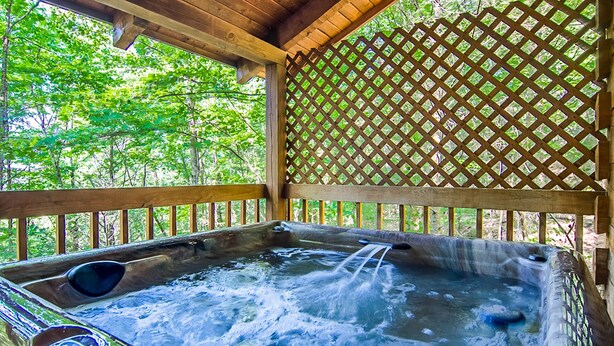 A hot tub with a wooden deck and lattice wall, surrounded by trees. - Secluded,-Private,Free WIFI,Pool Table,Hot Tub, Jacuzzi, 400 Game Arcade  (Pigeon Forge)