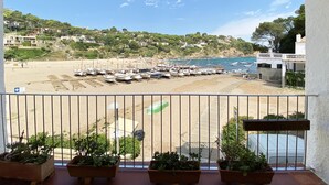 Un balcón con plantas en macetas, con vistas a una playa con barcos y un pueblo costero.