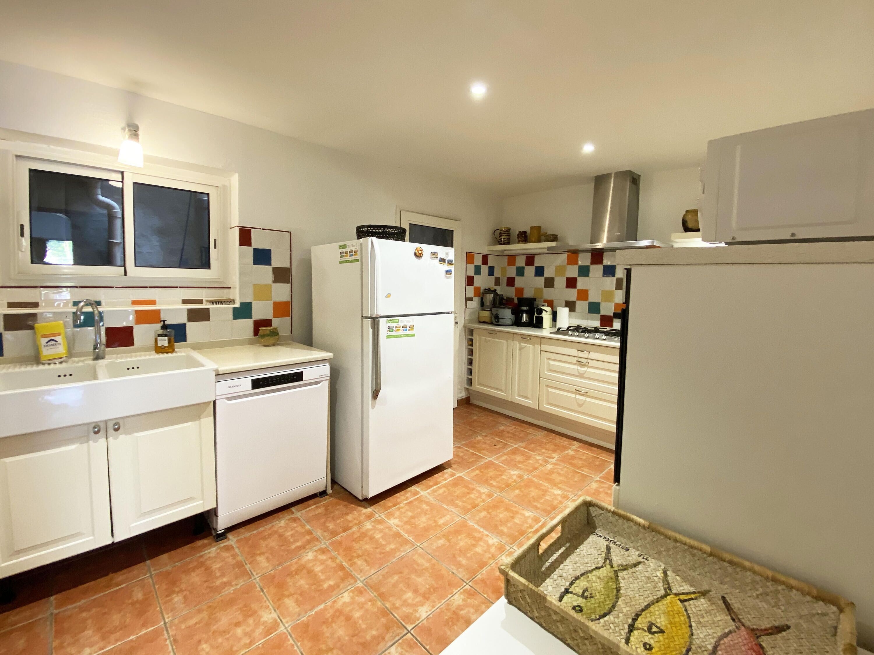 Cocina compacta con armarios blancos, lavavajillas integrado, refrigerador y estufa.