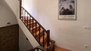 Una escalera con barandillas de madera que conduce a un piso superior. Un cuadro enmarco muestra a una mujer con traje tradicional.