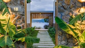 A stone pathway leading to a beach with a view of the sea and mountains in the distance.