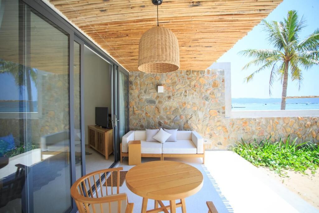 Un espacio exterior moderno con un muro de piedra, techo de madera, un sofá blanco y una mesa redonda de madera.