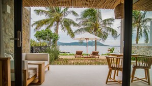 A view from a room with a glass door to a patio with a pool, two wooden chairs, a table, and an umbrella.