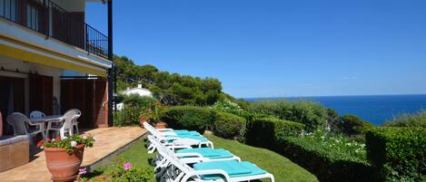 Une terrasse avec des chaises longues, des plantes en pot et une vue sur la mer.