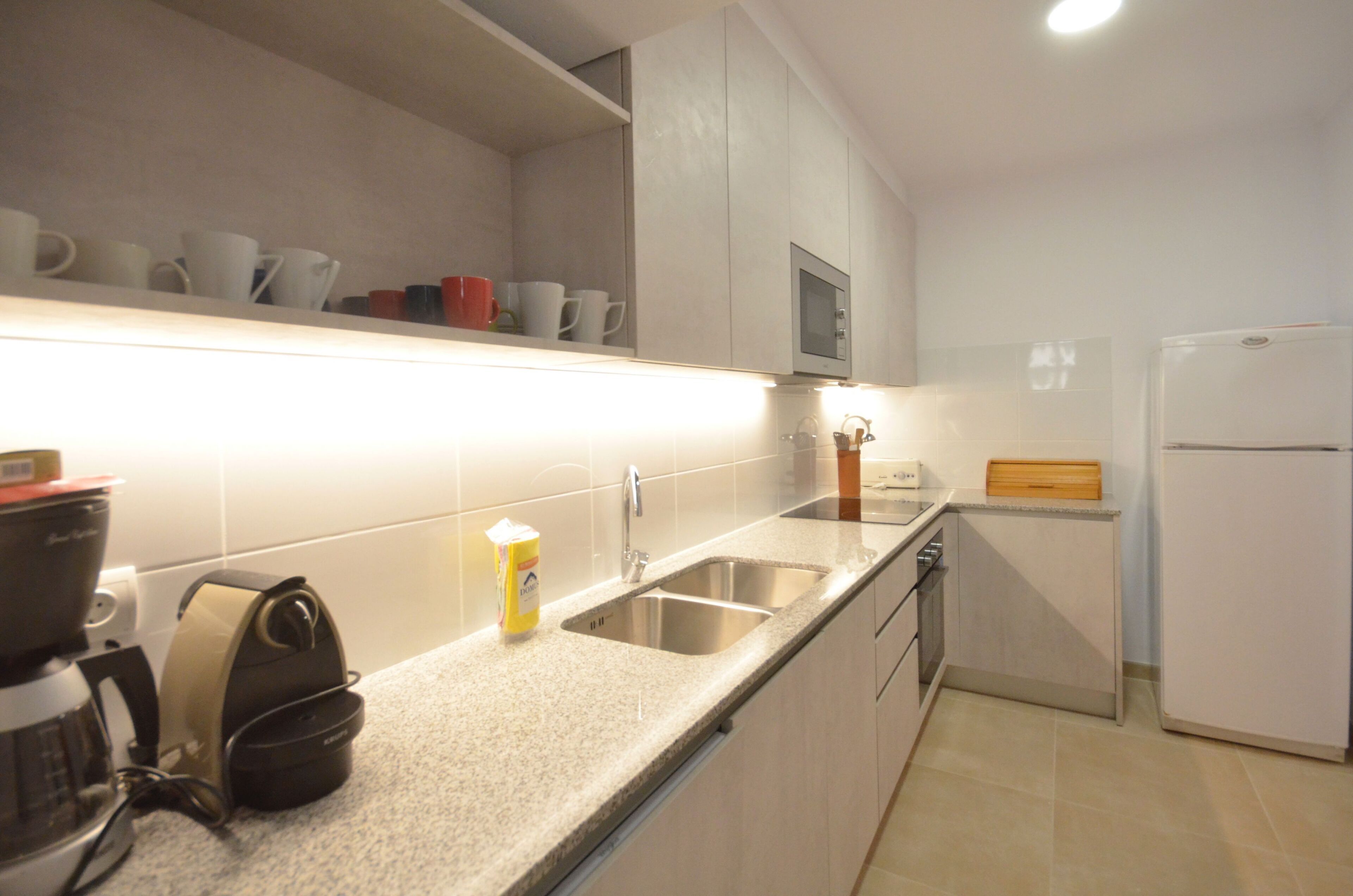 A kitchen with a granite countertop, stainless steel sink, and a white refrigerator. - Holiday rental apartment with swimming pool in Begur, Aiguablava (Begur)