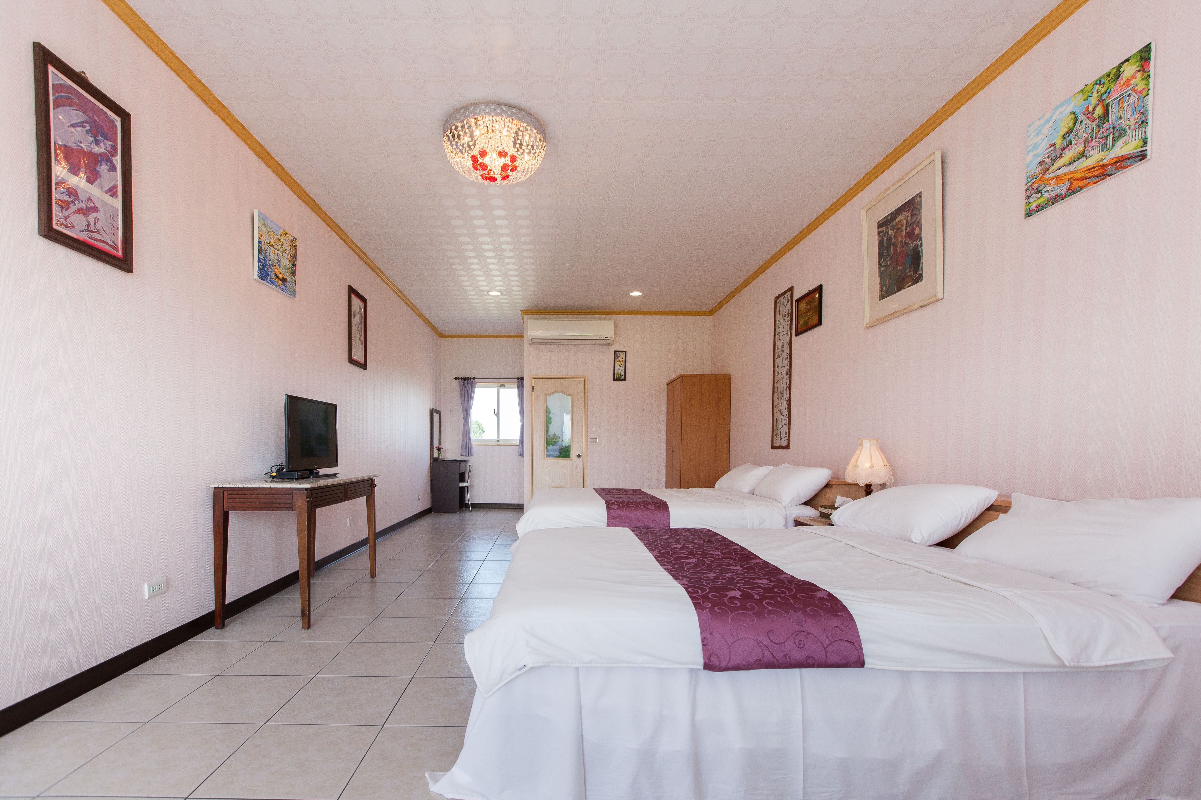 A hotel room with two beds, a television, a desk, and artwork on the walls.
